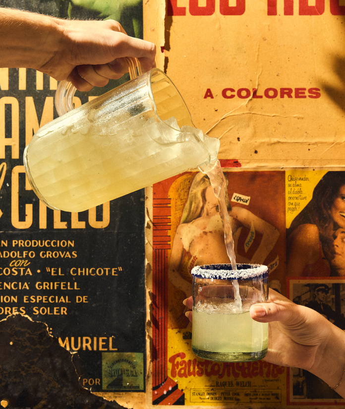Person pouring a yellow drink into a margarita glass with salt rim over a vintage movie poster.