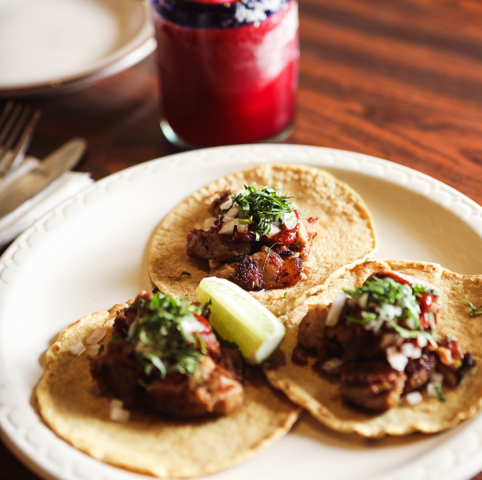 Plate of three tacos topped with meat and cilantro, served with a red margarita.
