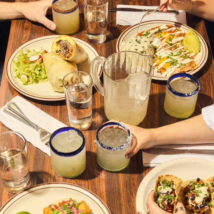 People enjoying a meal with tacos, burritos, and margaritas on a wooden table.